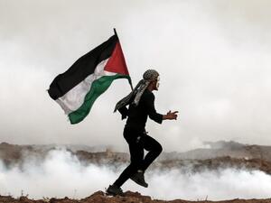 A Palestinian man holds the national flag as he runs through teargas during a protest, on the eastern outskirts of Gaza City, near the border with Israel. (MAHMUD HAMS / AFP)