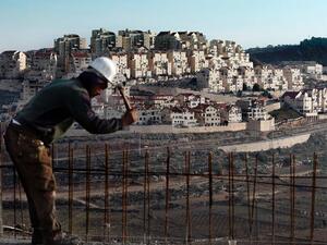 A man works on a construction site in Bethlehem, Palestine, as illegal settlements tower in the distance (AFP / AHMAD GHARABLI)