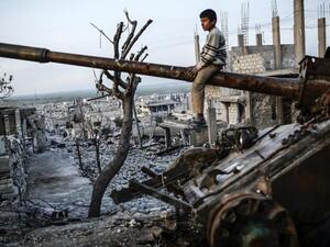 A Syrian Kurdish boy sits on a destroyed tank in the Syrian town of Kobane, also known as Ain al-Arab, on March 27, 2015. (AFP/Yasin Akgul)