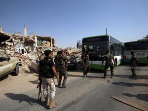 Syrian troops stand guard as a bus carrying people drives by, as part of an evacuation from the town of Daraya outside the capital Damascus on August 26, 2016 (AFP/Youssef Karwashan)