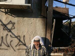 A Palestinian man stands next to a graffiti reading "Revenge," after a house was set on fire by Jewish settlers in the West Bank, July 31, 2015. (AFP/File)