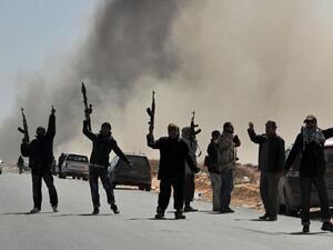 Libyan rebel fighters defiantly raise their weapons after a bomb dropped by an airforce fighter jet explodes. (AFP/Roberto Schmidt)