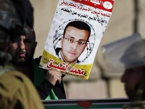 A protester holds up a poster of Mohammed Al Qiq as Israeli soldiers look on. (AFP/File)