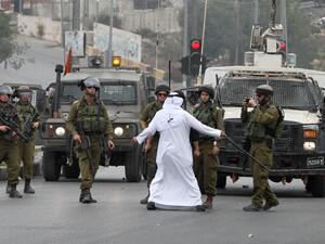 An elderly Palestinian man acts as a human barrier between Israeli security forces and Palestinian stone throwers during clashes following Friday prayers in the West Bank town of Hebron. (AFP/File)