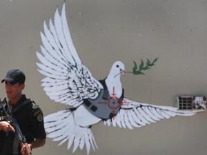 An Israeli solider stands by iconic Banksy grafitti on the Israeli separation barrier that runs through Bethlehem. Getty Photo 