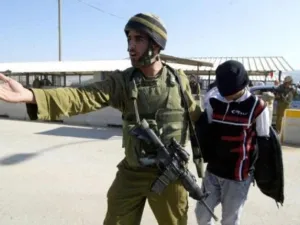 جندي إسرائيلي يعتقل شابا فلسطينيا صغير السن على أحد الحواجز العسكرية