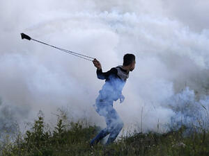 A Palestinian protester uses a slingshot to throw a tear gas canister back during clashes with Israeli security forces. (AFP/File)