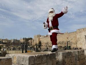 A Palestinian man wears a Santa Claus costume as he walks atop Jerusalem's Old City walls, on December 23, 2016, as Christians around the world prepare to celebrate the holy day. (AFP/Ahmad Gharabli)