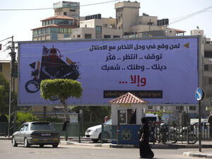 A woman walks past a billboard in Gaza put up by the Hamas authorities warning collaborators to stop their activities. (AFP/Mohammed Abed)