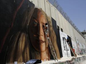 Italian artist Jorit Agoch (L) paints mural depicting jailed Palestinian teenager Ahed Tamimi next to another artist on Israel's controversial separation barrier in the West Bank city of Bethlehem, July 25,2018 (AFP/ File)
