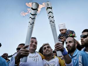 President of the Hellenic Olympic Committee Spyros Kapralos (L) hands over the Olympic Flame to Syrian refugee Ibrahim al-Hussein (C), 27, an amputee swimmer
LOUISA GOULIAMAKI / AFP