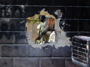 Israeli security guard peering through a hole of Israel's  separation barrier by Palestinian youth in the Abu Dis neighrbood, bordering Jerusalem on July 9, 2013. [Abbas Momani/Getty Images]