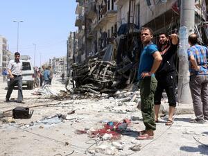 Syrians stand next to debris and bloodstains following bombardment by government forces on the Salhin district of the northern city of Aleppo on July 21, 2016. (AFP/Thaer Mohammed)