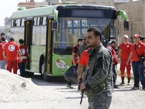 A Syrian soldier stands guard as Red Crescent members wait for opposition fighters and their families to change buses at a Syrian army checkpoint on the edge of the rebel-held Waer neighbourhood in the central city of Homs during an evacuation operation on September 22, 2016. (AFP/Louai Beshara)