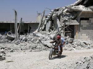 A Syrian man rides his motorcycle past collapsed buildings in the northern Syrian town of Manbij as civilians go back to their homes on August 14, 2016. (AFP/Delil Souleilman)
