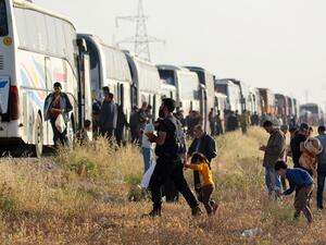 Syrian people walk near buses as a convoy carrying opposition fighters and their families from rebel held areas south of Damascus arrived near al-Bab. (Rami al SAYED / AFP)
