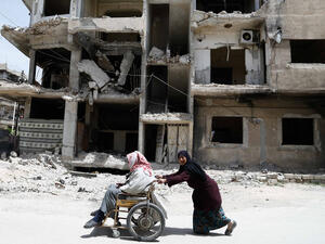 A woman pushes her elderly husband in a wheelchair in opposition-held Hamouria, in the eastern Ghouta region on the outskirts of the capital Damascus on April 26, 2017. (AFP/Abdulmonam Eassa)