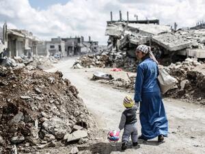 A Kurdish Syrian woman walks with her child past the ruins of the town of Kobane. (AFP/ File Photo)