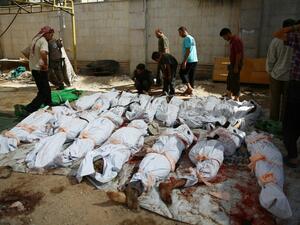 Syrians and emergency personnel gather around dead bodies wrapped in shrouds following air strikes in Douma. (AFP/ File)