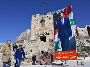 United Nations (UN) High Commissioner for Refugees Filippo Grandi (L) walks past a poster of Syrian President Bashar al-Assad as he visits the old city of the northern Syrian city of Aleppo on February 1, 2017. (AFP/George Ourfalian)