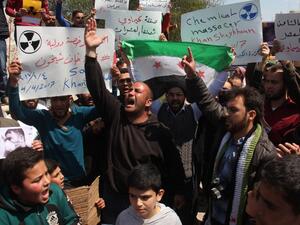Syrian residents of Khan Sheikhun hold placards and pictures on April 7, 2017 during a protest condemning a suspected chemical weapons attack on their town earlier this week that killed at least 86 people, among them 30 children. (AFP/Omar Haj Kadour)