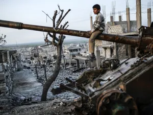 A boy sits on top of a destroyed tank in Syria, AFP/File
