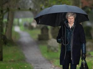 Britain's Prime Minister Theresa May shelters from the rain under an umbrella. (AFP/ File Photo)