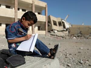 A Yemeni boy school writes as he sits outside a school on March 16, 2017, that was damaged in an air strike in the southern Yemeni city of Taez. (AFP/Ahmad al-Basha)