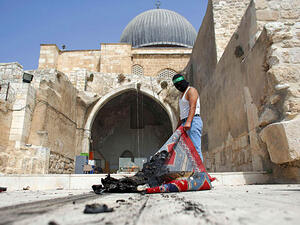A masked Palestinian wearing a Hamas headband takes a burnt carpet out of Al-Aqsa mosque in Jerusalem's Old City during clashes at the compound. (AFP/File)