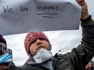 An Iranian migrant with sewn lips holds a placard reading "we are humans" as he protests during the demolition of the southern part of the so-called "Jungle" migrant camp, on March 2, 2016, in Calais. (AFP/Philippe Huguen)