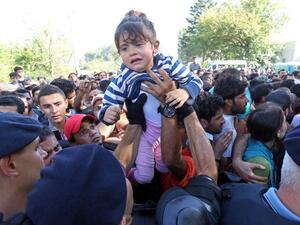 A man passes a child over to a police officer as they direct migrants and refugees onto buses at the train station in the city of Tovarnik, close to the Croatian-Serbian border, on September 17, 2015. (AFP/File)