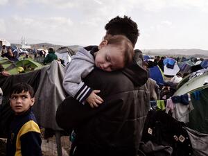 A baby sleeps in the arms of a man in the makeshift refugee and migrant camp at the Greek-Macedonian borders on March 1, 2016, where thousands are stranded due to travel restrictions on migrants. (AFP/Louisa Gouliamaki)