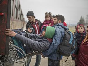 A man helps another young man in a wheelchair as migrants and refugees board a train after crossing the Greek-Macedonian border, near Gevgelija, on February 24, 2016. (AFP/Robert Atanasovski)