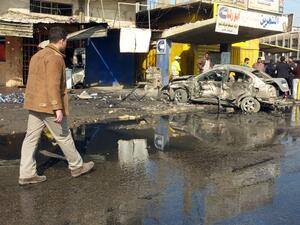 An Iraqi man walks past the site of a car bomb in central Baghdad, on January 15, 2014. [AFP]