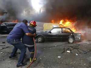 A firefighter is helped as he extinguishes fire at the site of an explosion in Beirut's southern suburb neighbourhood of Bir al-Abed on July 9, 2013. (Source: AFP/STR)