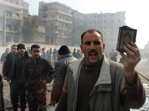 A Syrian man holds up a copy of the Quran, Islam's holy book, at the scene of a reported airstrike by government forces on the central al-Fardous neighbourhood of the northern Syrian city of Aleppo on January 21, 2014. (AFP)