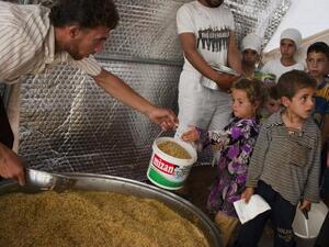 A volunteer shares out food to the people in the Bab al-Salam refugee camp for displaced Syrians near the border with Turkey on 2 July 2013. (AFP/File)