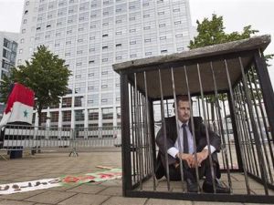 رجل يرتدي قناعا للرئيس السوري يجلس في قفص اتهام اثناء احتجاج ضد الحكومة السورية امام المحكمة الجنائية الدولية في لاهاي
