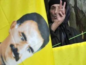مناصرة لعبد الله اوجلان زعيم حزب العمال الكردستاني تقف خلف صورته وترفع يدها باشارة النصر