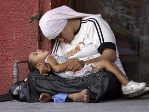 A Syrian refugee holds her child as they doze off at a street in the southern Lebanese city of Sidon. (AFP)