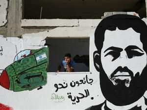 A Palestinian youth stands behind a wall sprayed with graffiti in Gaza City depicting 31-year-old Muhammad Allaan. (AFP/Mohammed Abed)