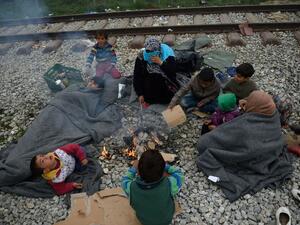 Refugees keep warm near a fire at a makeshift camp at the Greek-Macedonian border, near the Greek village of Idomeni on March 18, 2016, where thousands of refugees and migrants are stranded by the Balkan border blockade. (AFP/Daniel Mihailescu)