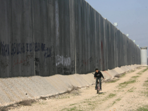 A Palestinian boy rides his bicycle past a separation wall in the West Bank. (AFP/File)