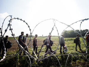 Refugees walk near the border fence between Hungary and Serbia (AFP/FILE)