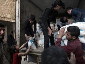 Syrian children carry sacks of wheat, provided by the World Food Programme (WFP), in Kafr Batna, in the rebel-held Eastern Ghouta area, outside Damascus on March 1, 2016. (AFP/Amer Almohibany)