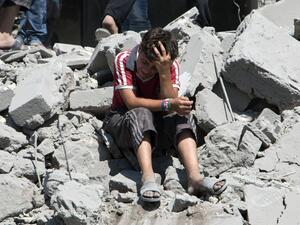 A young Syrian boy cries as he sits on the rubble after a missile fired by Syrian government forces hit a residential area in the northern Syrian city of Aleppo on July 21, 2015. (AFP/Karam al-Masri)