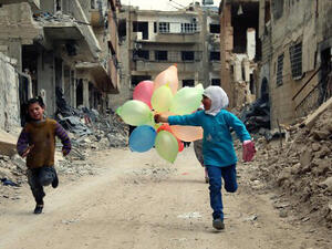 Syrian children run with balloons past heavily damaged buildings in the neighbourhood of Jobar, on the eastern outskirts of the Syrian capital Damascu. (AFP/File)