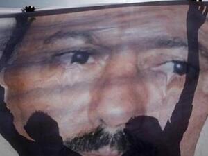 متظاهرون يقومون بفرد ملصق كبير لصالح استعدادا لتمزيقه خارج جامعة صنعاء