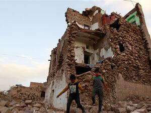 This March 23, 2016 file photo shows Yemeni children walking on stones in front of buildings that were damaged by Saudi airstrikes in the capital Sana’a. (AFP/File)
