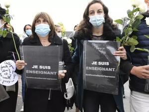 أشخاص يحملون لافتات كتب عليها "أنا مدرّس -- حرية التعبير" أمام مدرسة في كونفلان سانت اونورين.